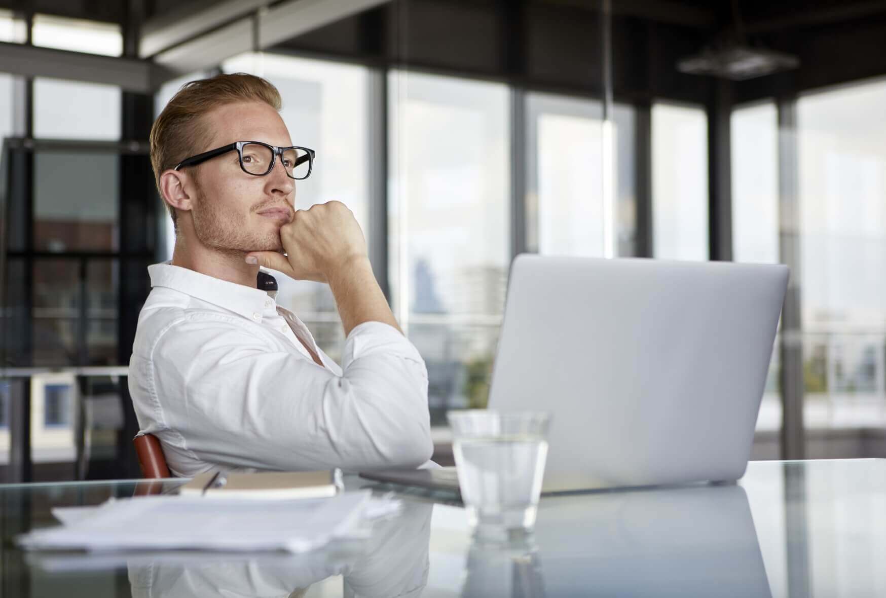 A businessman with laptop on desk in office thinking