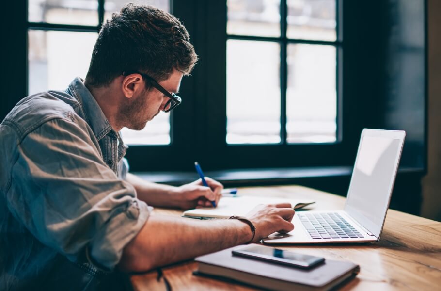 A man taking notes while using laptop