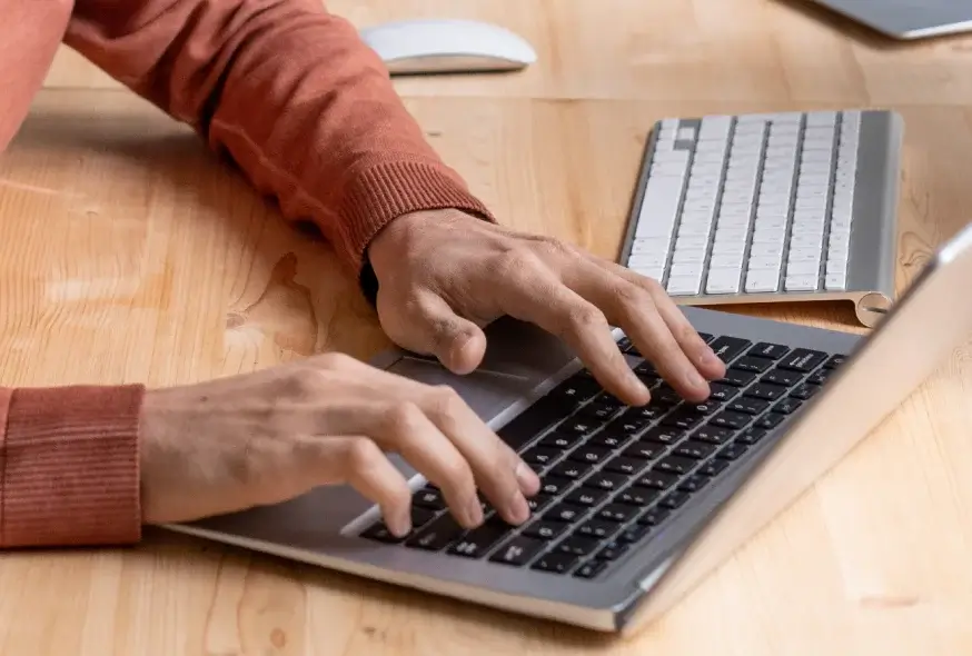 A person wearing maroon sleeves is using a laptop.