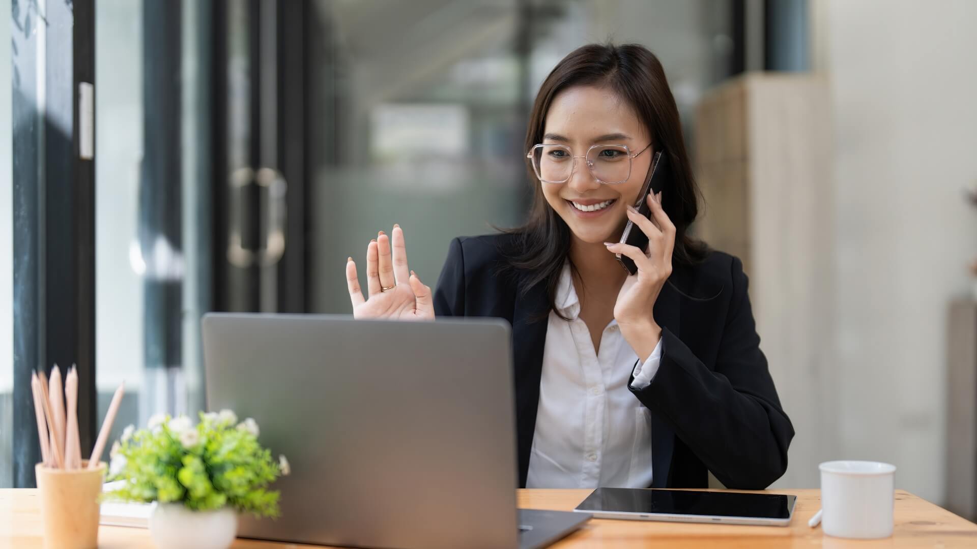 Asian businesswoman talking with client on mobile phone and working on laptop