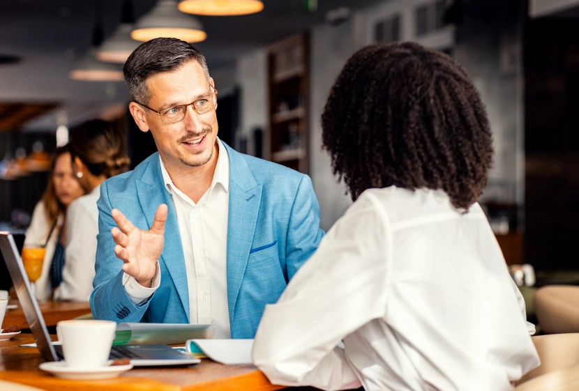Businessman and female coworker talking about work while using laptop in modern coffee shop