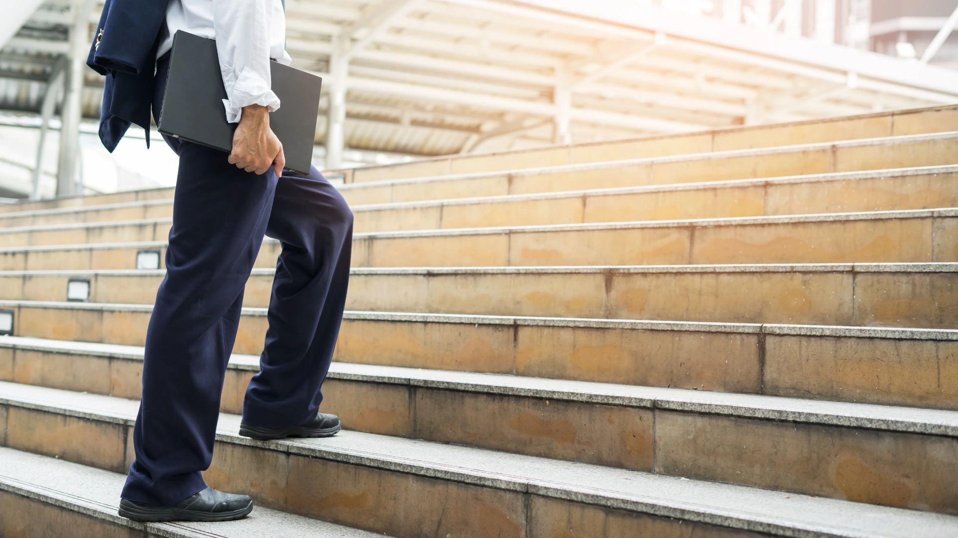 Businessman holding computer laptop walking up stairs to working