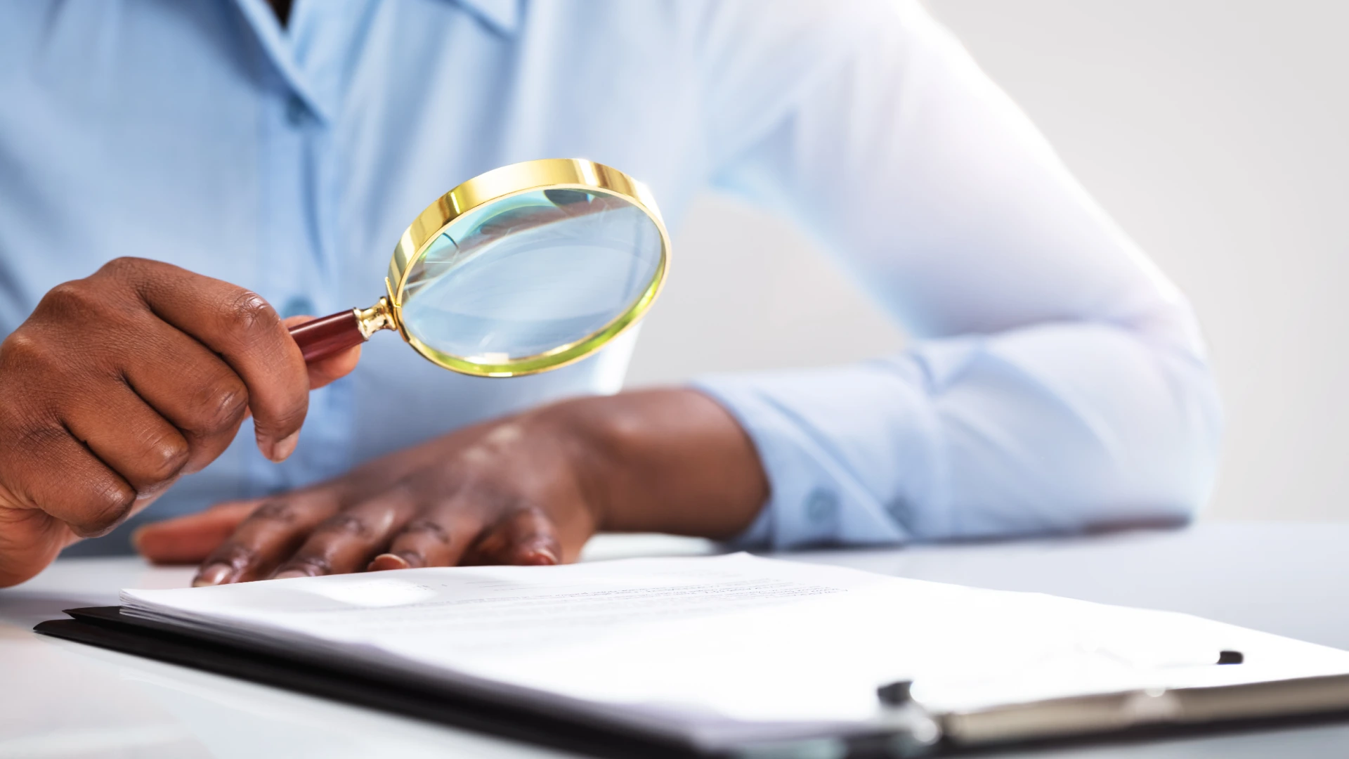 Close-up Of A Businesspersons Hand Looking At Contract Form Through Magnifying Glass