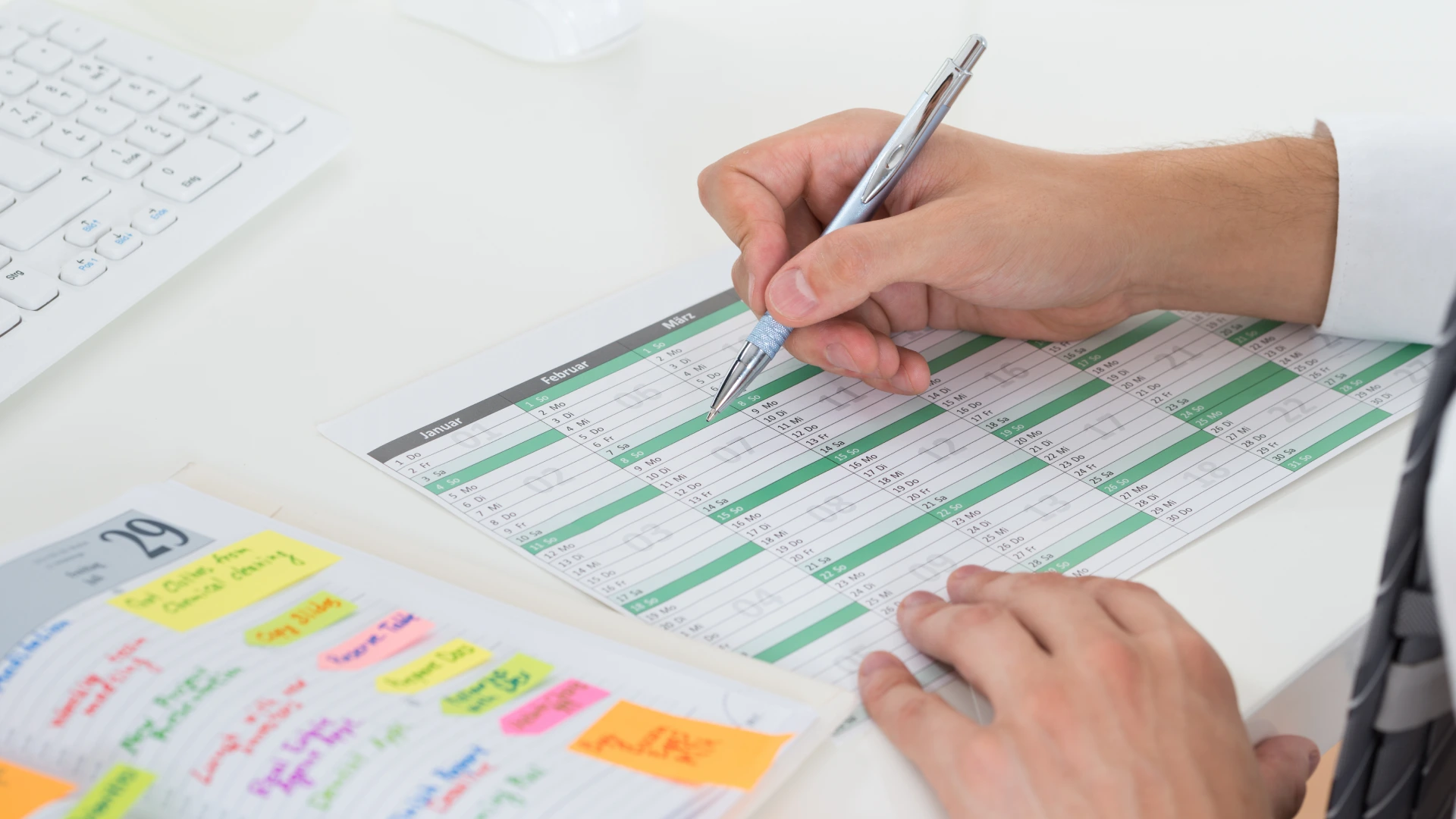 Close-up Of Businessman With Calendar Writing Schedule In Diary