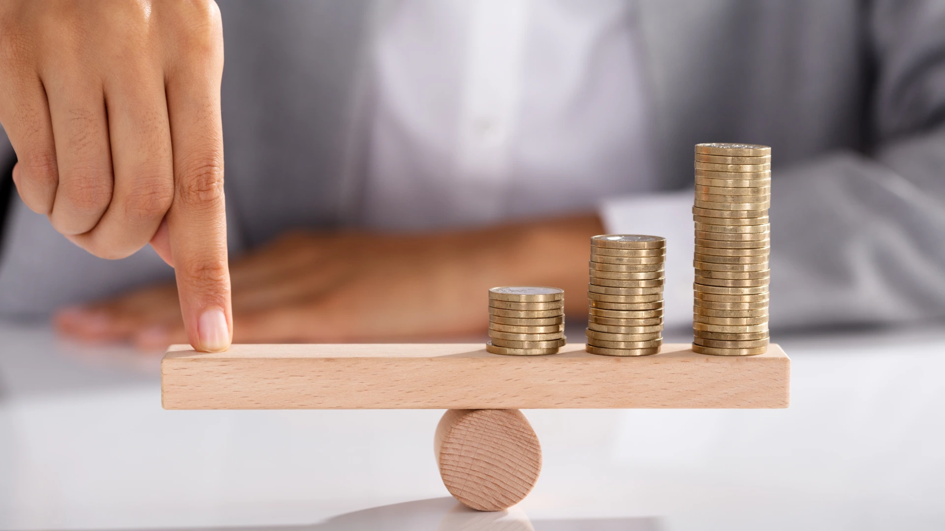 Close-up of Businessman Finger Balancing Stack of Coins on Wooden Seesaw