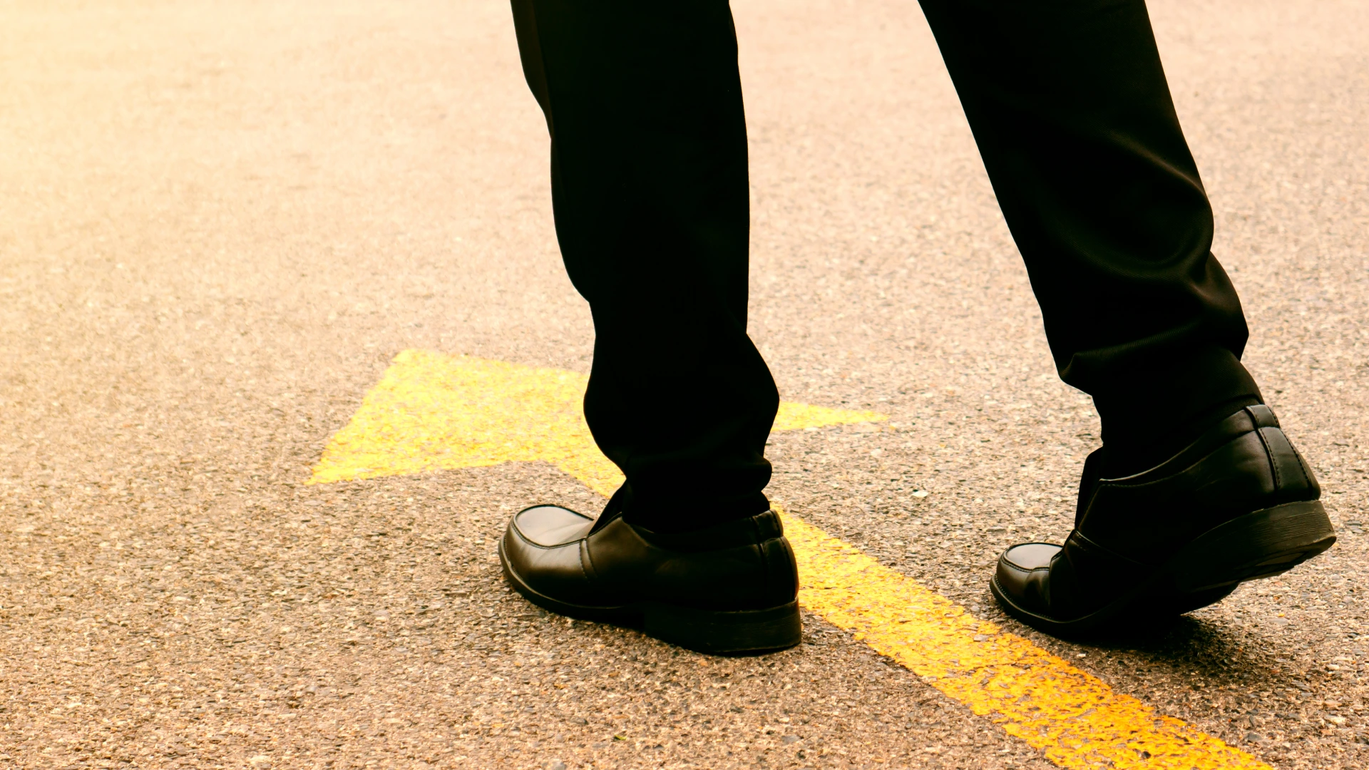 Concept of moving forward_ Black leather shoes on a tarmac road with yellow direction arrow.