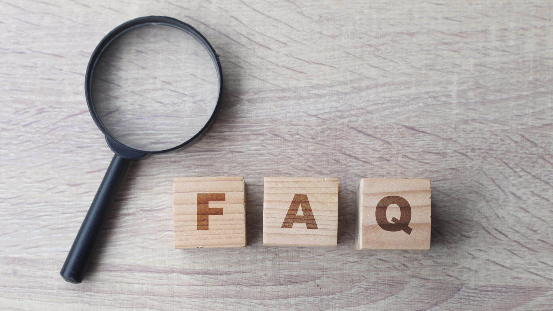 FAQ lettering with magnifying glass on wooden table