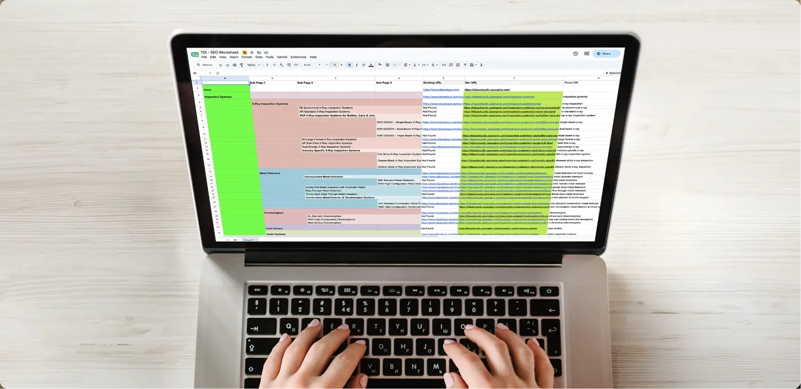 Person typing on a laptop displaying a color-coded spreadsheet