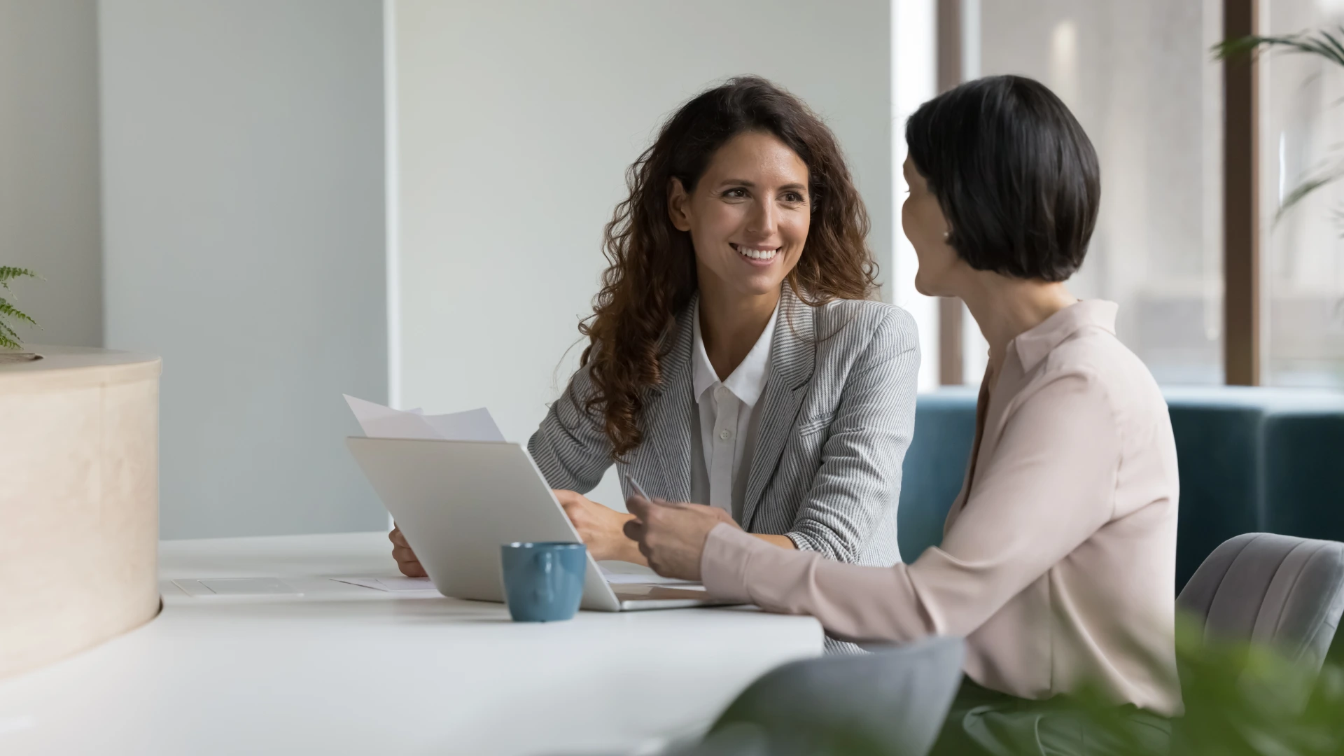 Two positive confident diverse business colleagues women talking at workplace