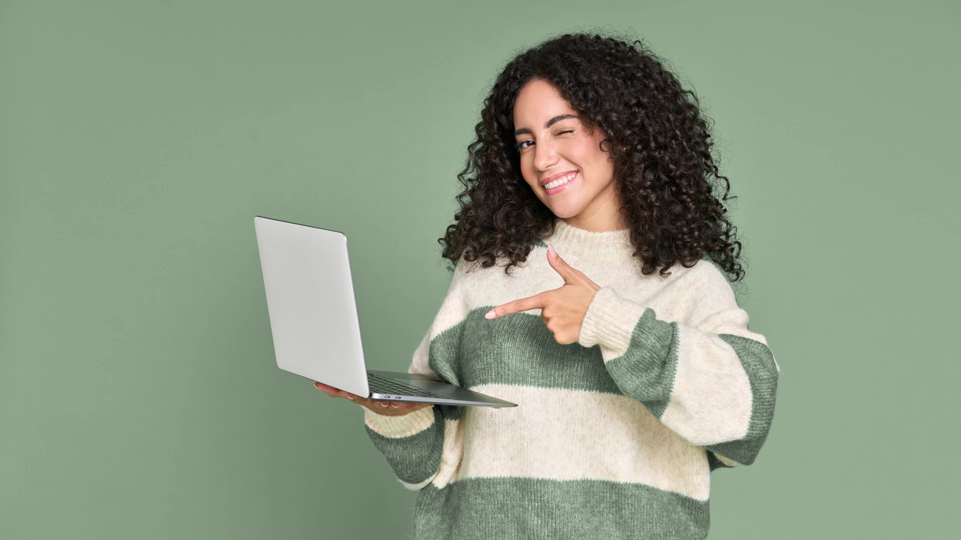 Young happy latin woman winking pointing at laptop