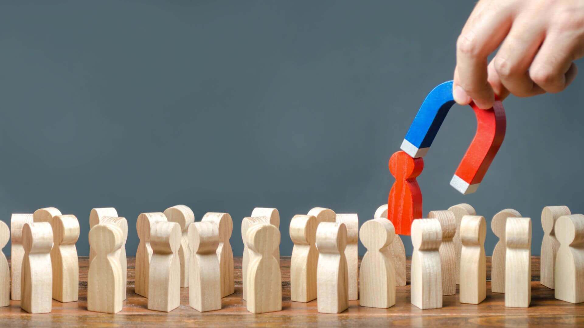 a hand with a magnet pulls a red human figure out of the crowd