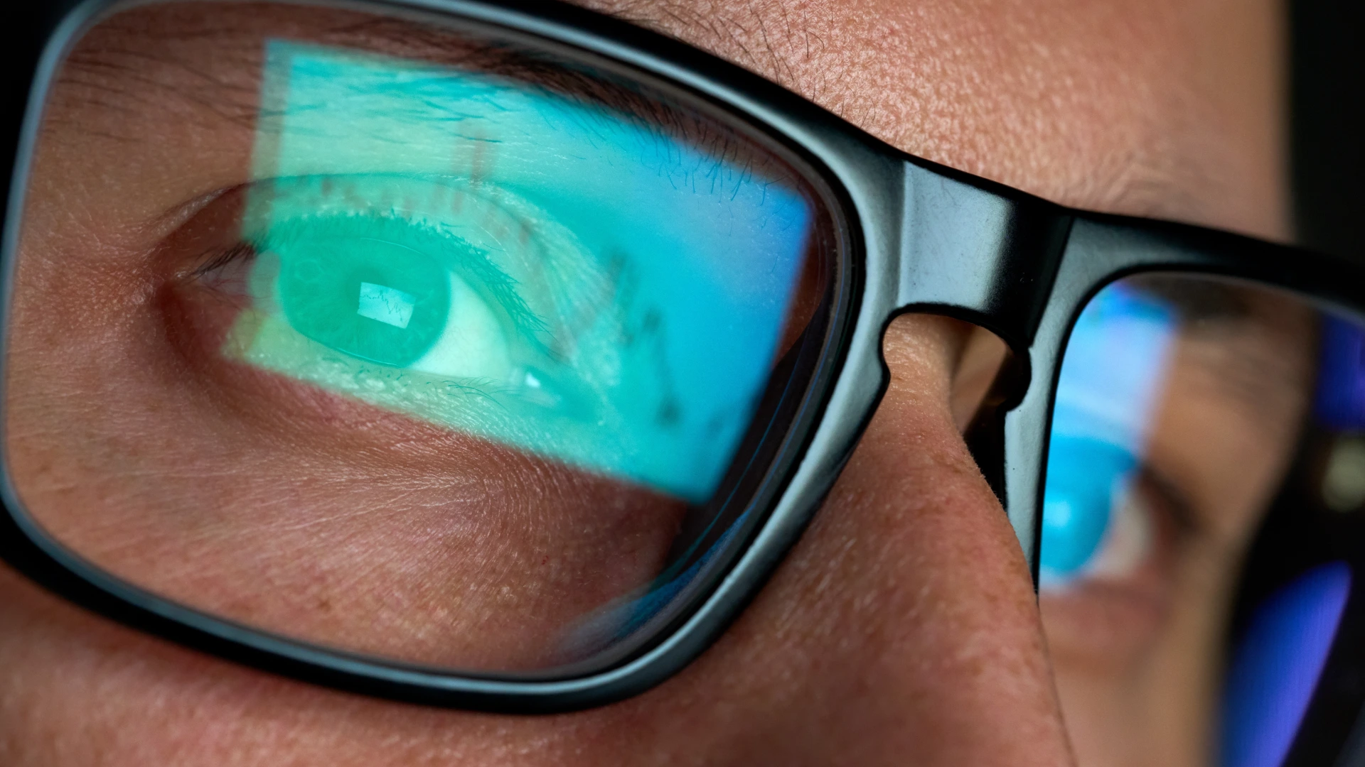 a man wearing eyeglasses working looking at computer screen reflecting in glasses analyzing something