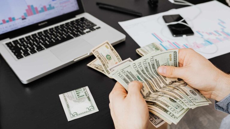 a person holding bank notes in front of a computer tracking costs