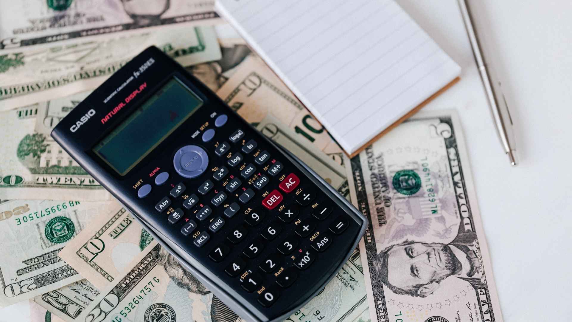 calculator and notepad placed on stacked dollar bills