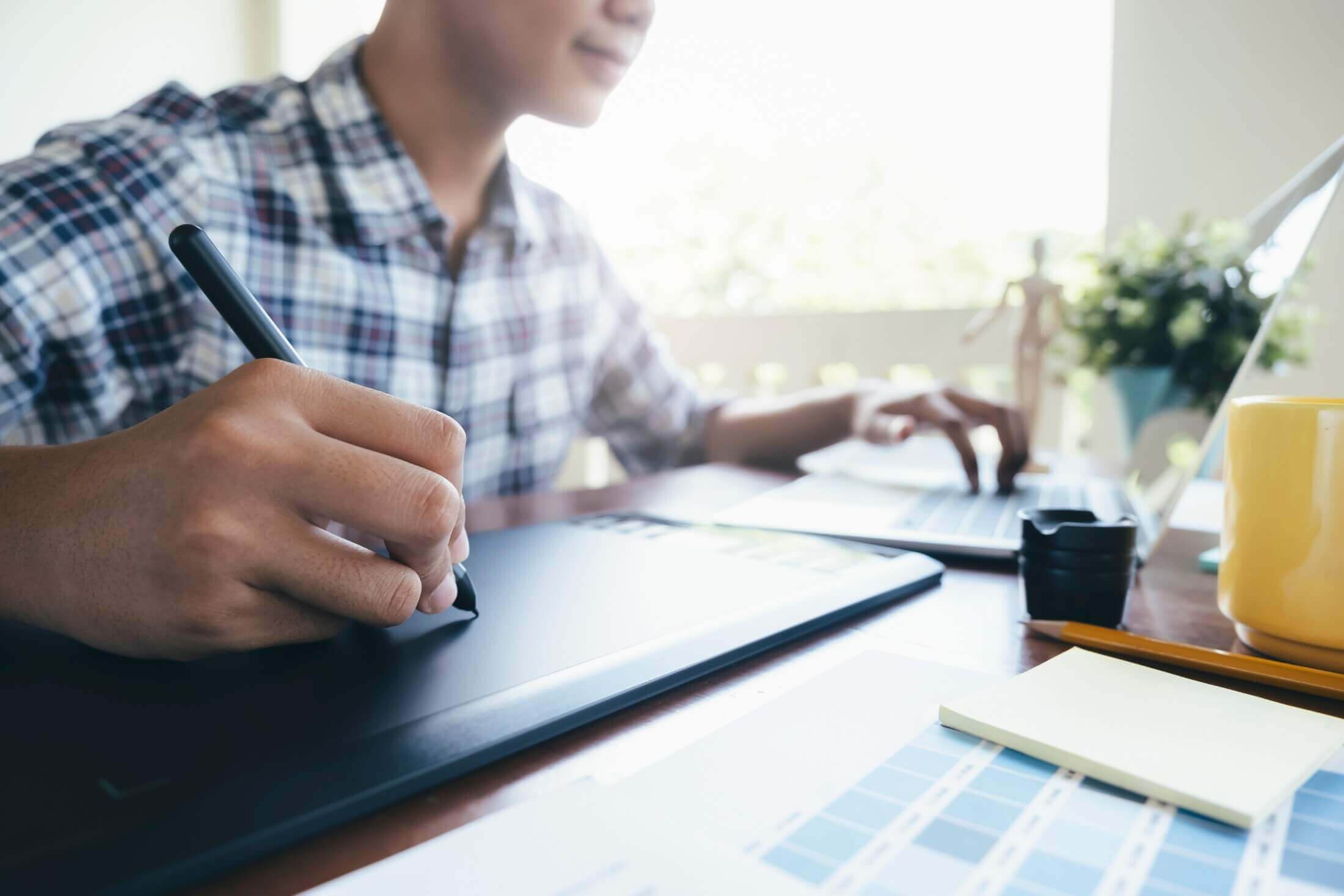 A designer sketching out logo concepts on a graphics tablet, with focus on the hand holding the stylus, in a bright and airy workspace.