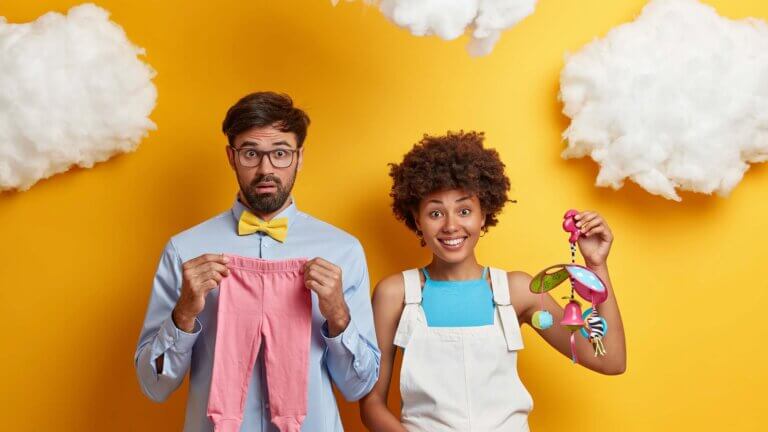 diverse-couple-expect-baby-pose-with-toys-and-clothes