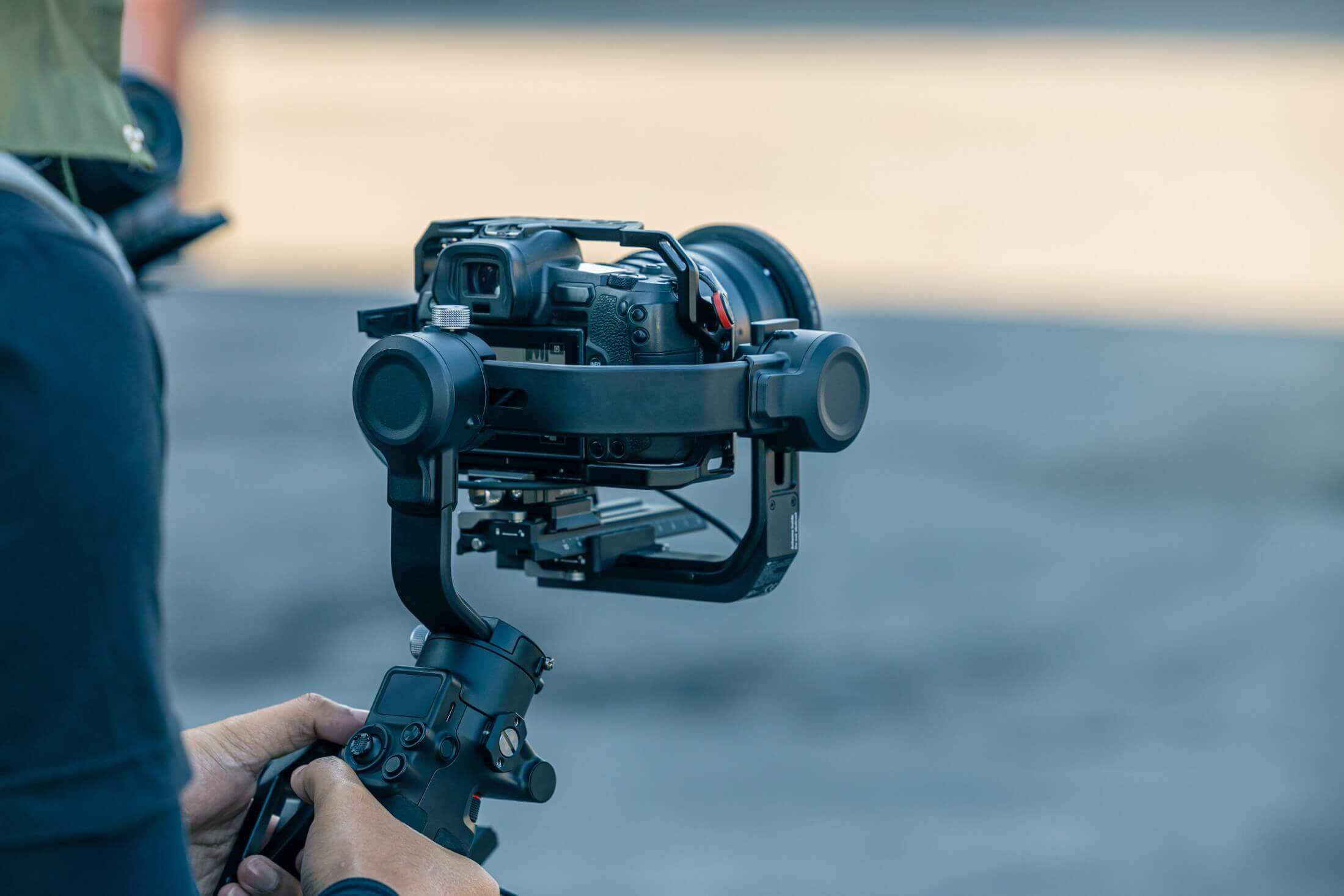 An image showing a person operating a gimbal stabilizer equipped with a mirrorless digital camera, set against an outdoor backdrop.