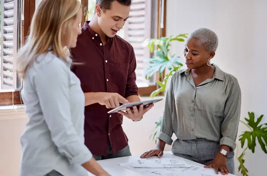 Group of three people discussing a project with a tablet and documents on the table