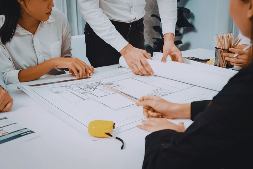 group of people sitting around a table looking at architectural plans