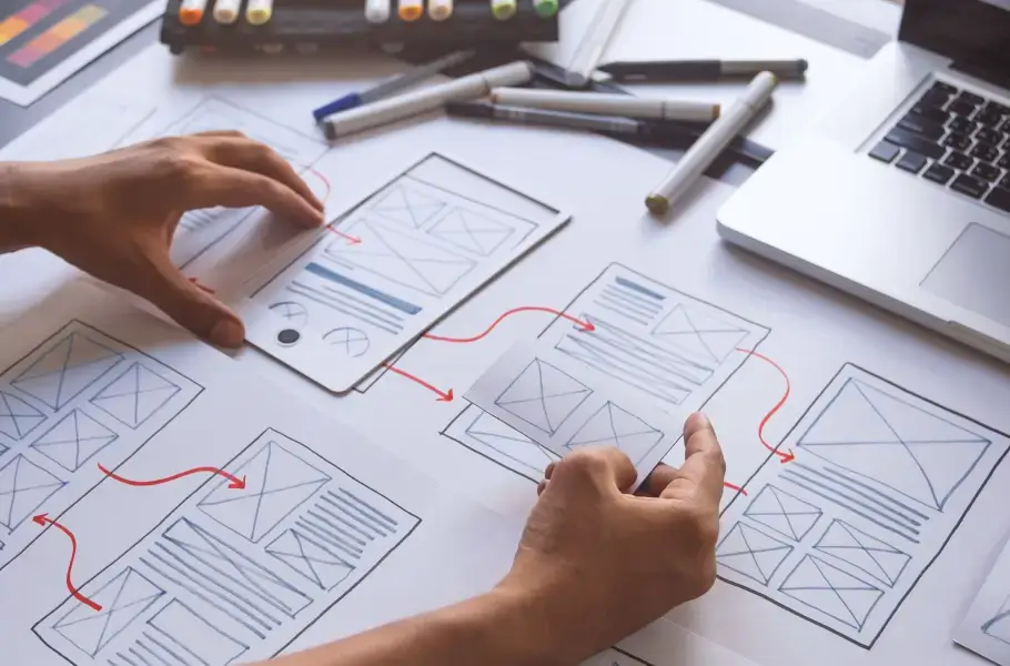 Hands arranging wireframes on a table with red arrows indicating flow