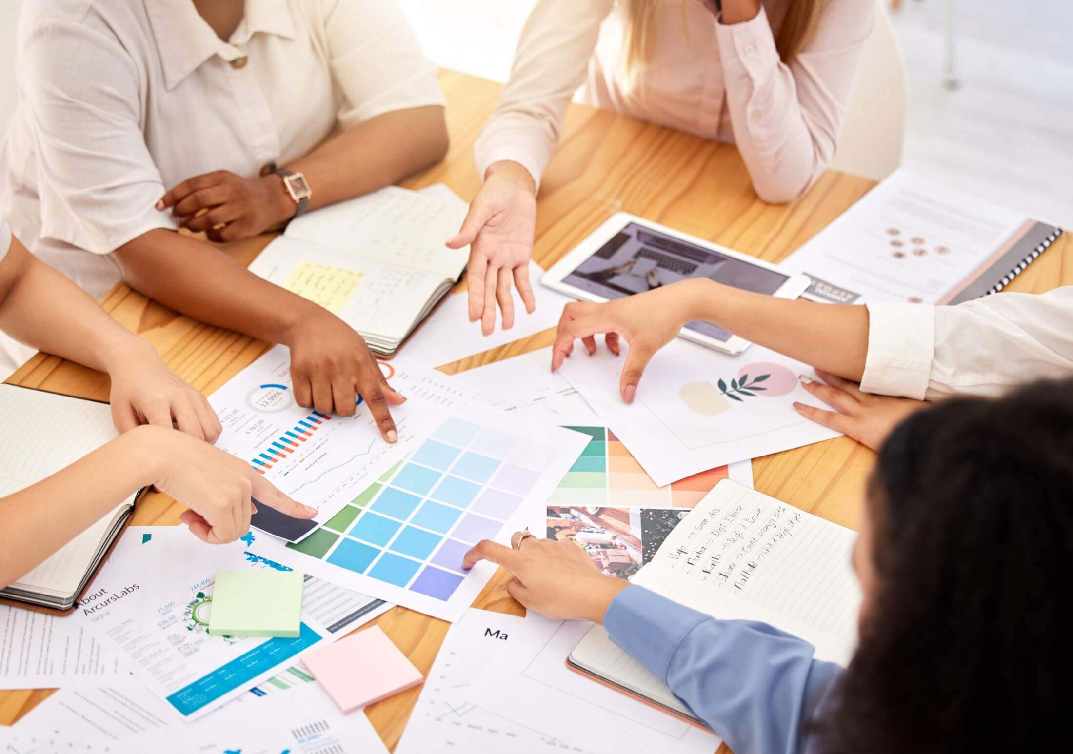 An image featuring a team of designers gathered around a table in a bright office space, discussing branding elements and logo designs, indicated by the various charts and color palettes on the table.