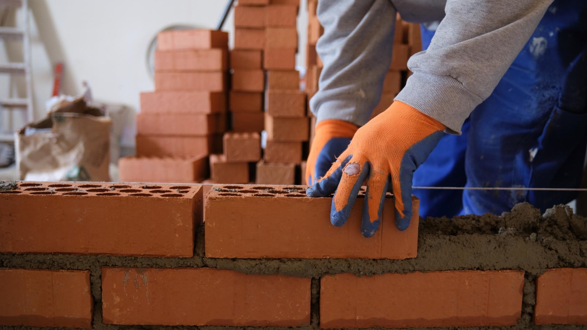 man laying bricks with worn out gloves