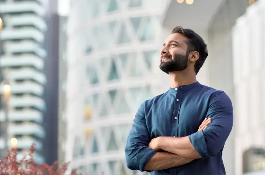 Man standing with arms crossed, looking up confidently in an urban setting