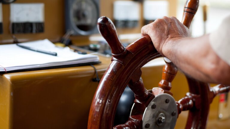 man with this hands on a ship steering wheel
