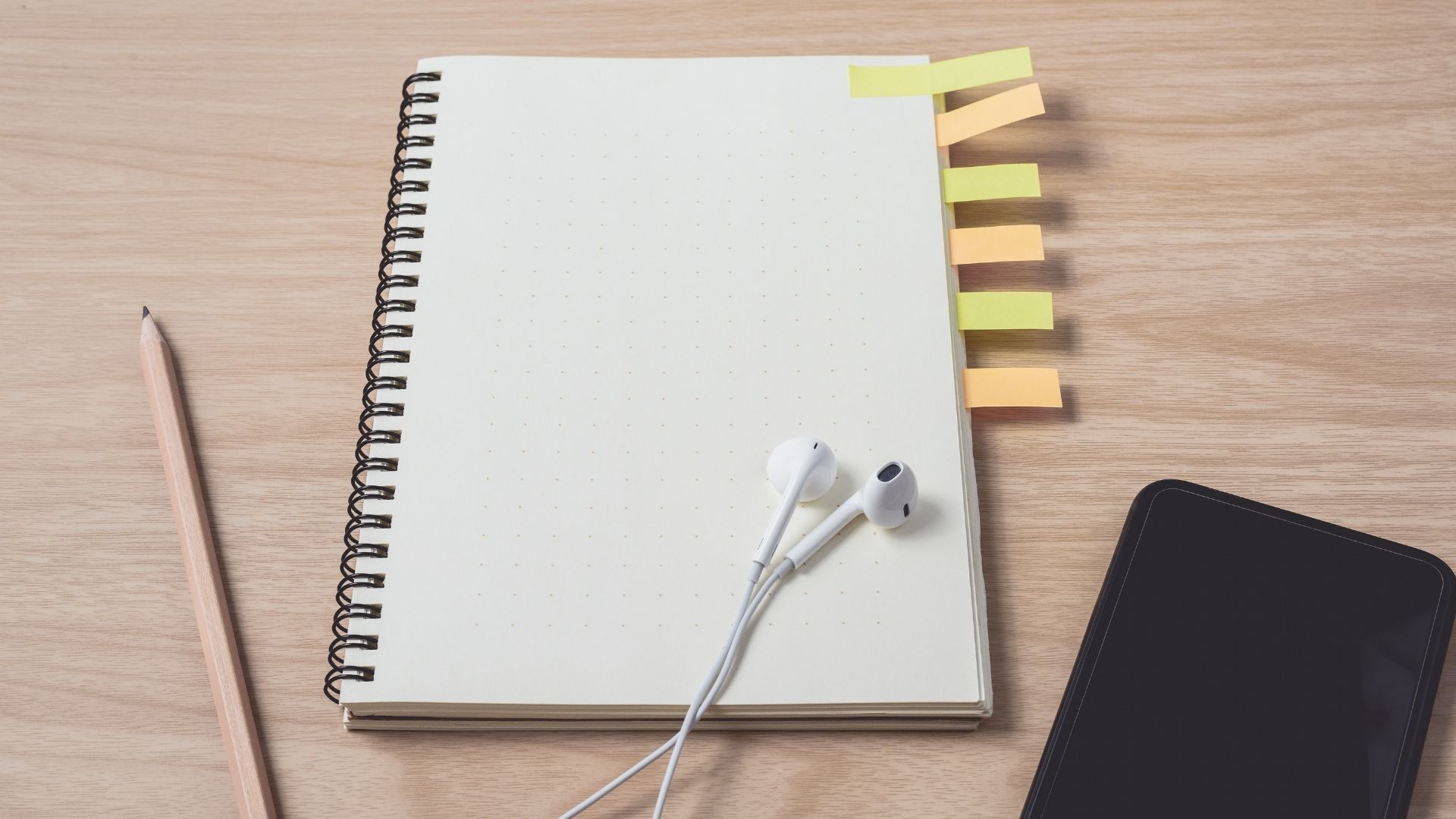 notebook pencil ear phones and phone in a table