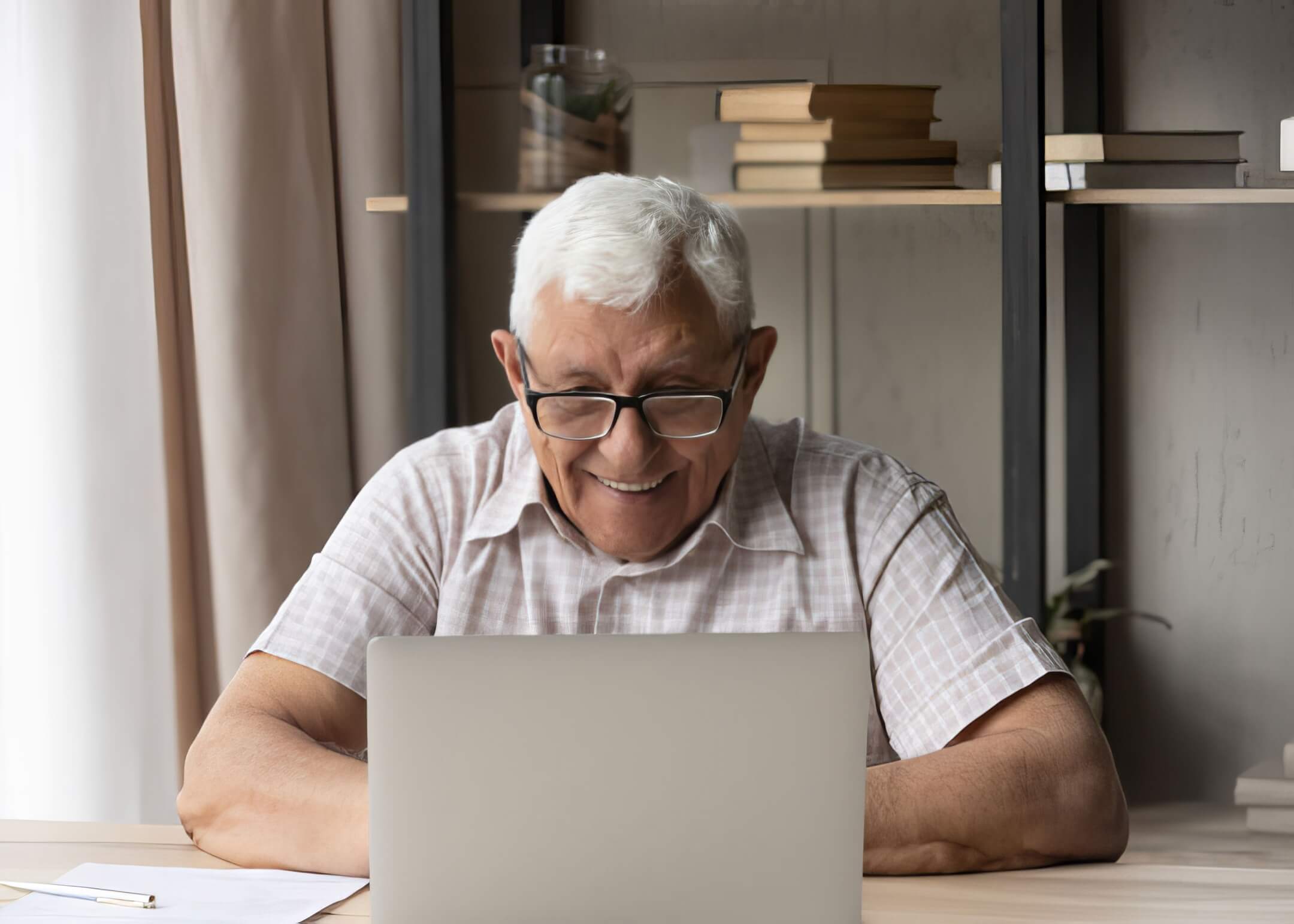 older man wearing glasses happily reading an article using laptop