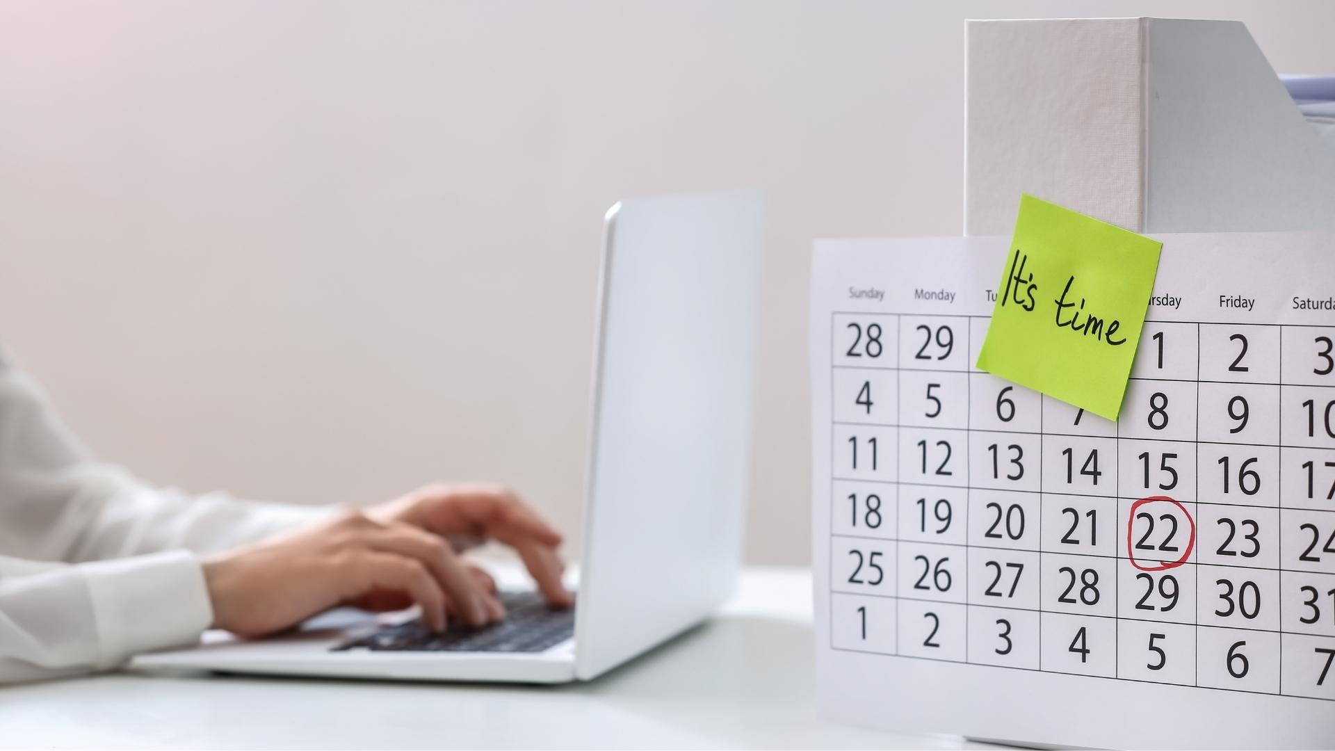 person typing on laptop and calendar with note on table