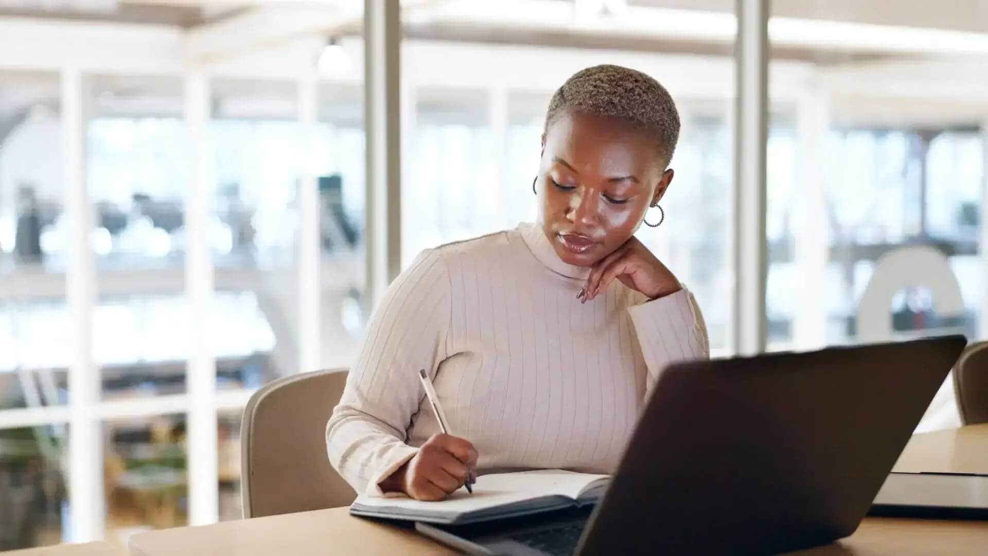 A focused professional woman taking notes while working on her laptop in a bright modern office space