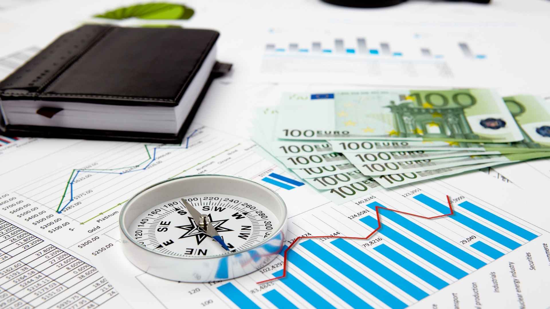 table with reports, a compass, dollar bills and a journal