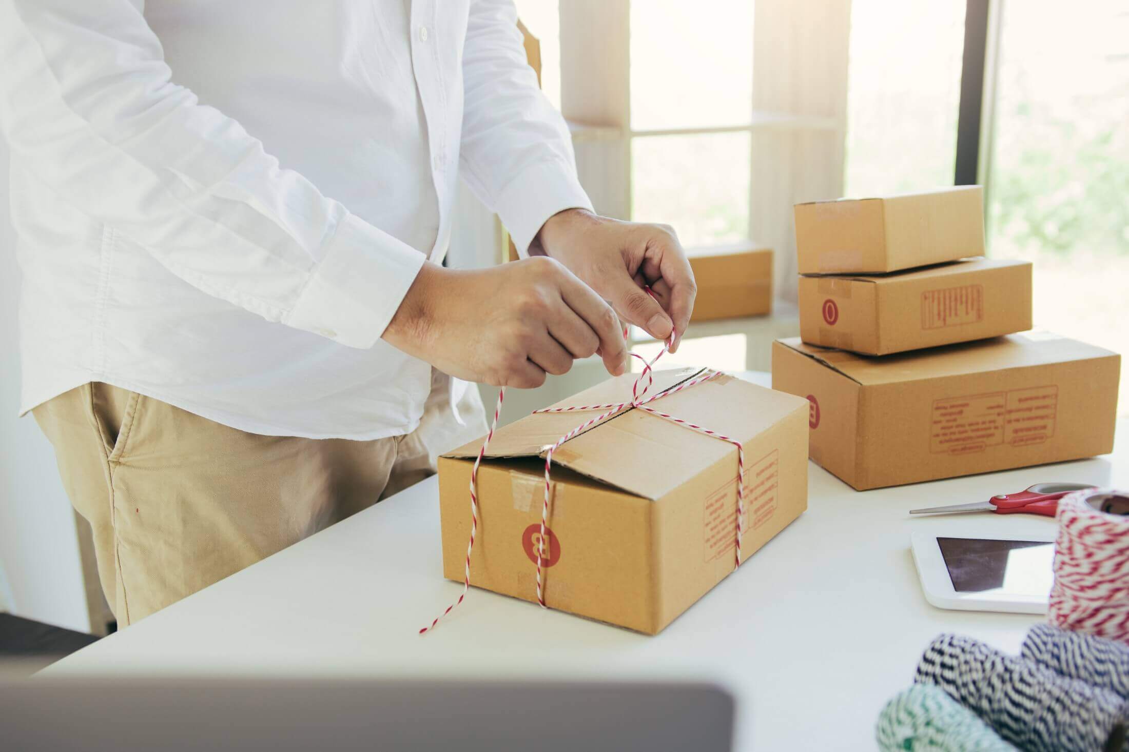 An entrepreneur tying a string around a packaged box, with multiple parcels ready for delivery, indicating small business product preparation.