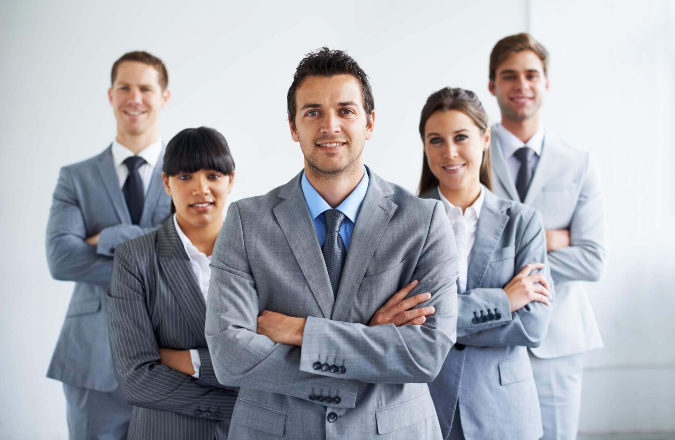 A confident business team posing together, with a man at the center crossing his arms, in a well-lit office environment, representing strong work ethic and unity.