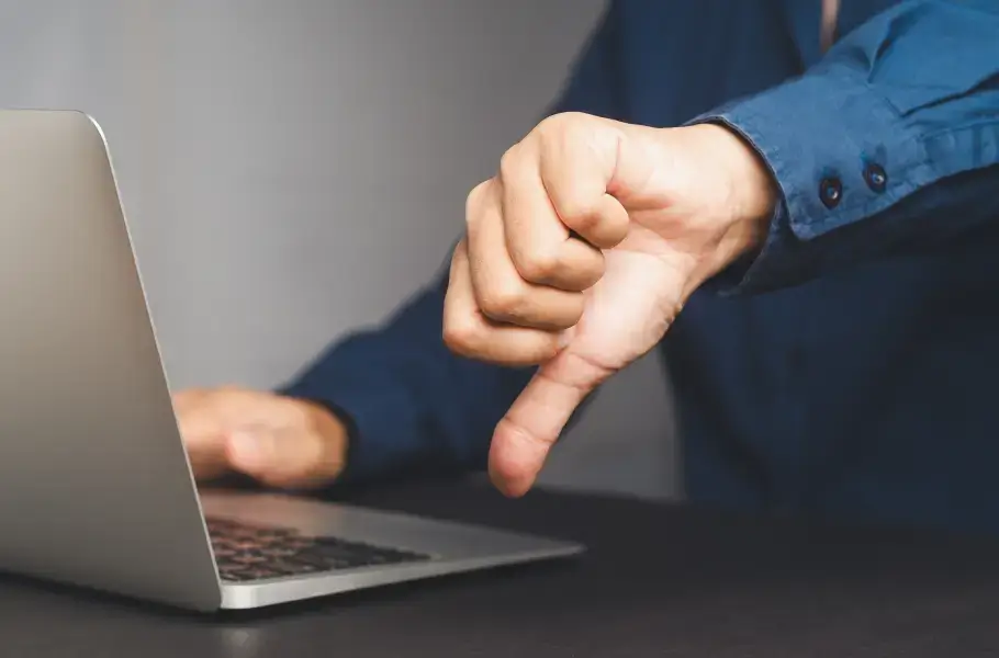 Person giving a thumbs down in front of a laptop