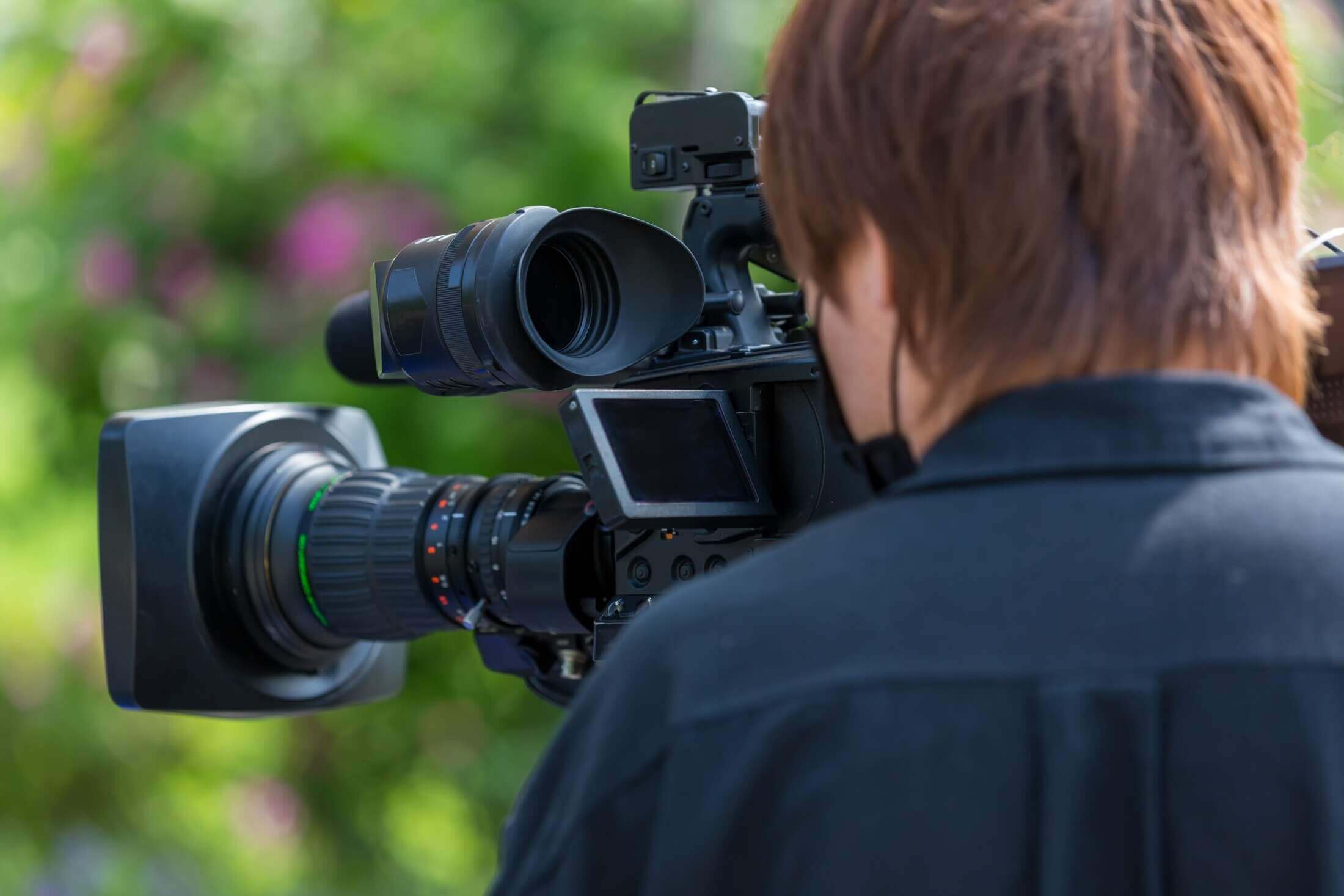 Behind-the-scenes of a videographer operating professional video camera equipment, capturing high-quality footage outdoors.