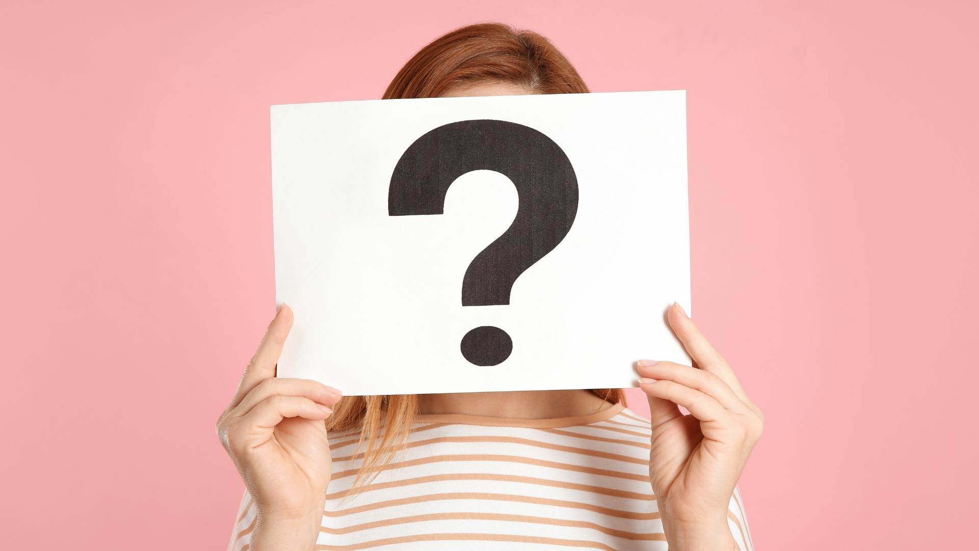 woman holding question mark sign on pink background