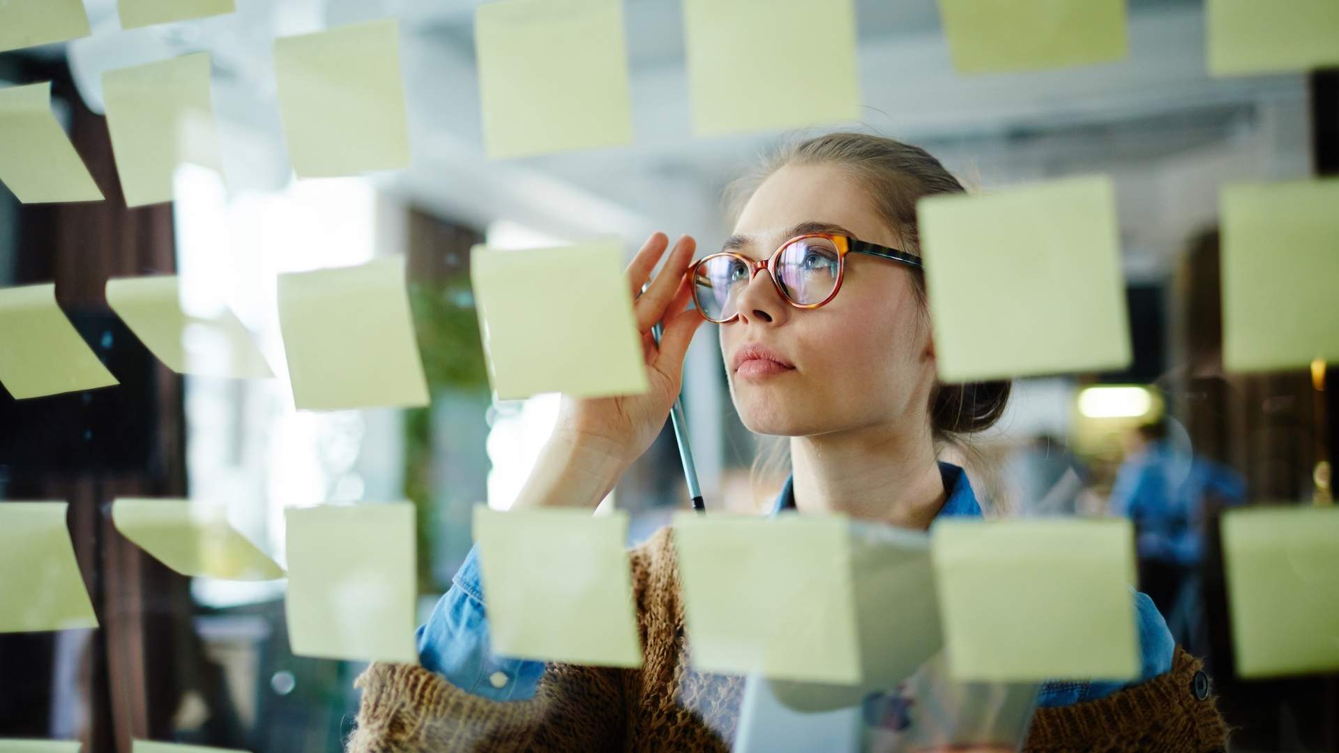 woman with glasses looking at the sticky notes in a glass board